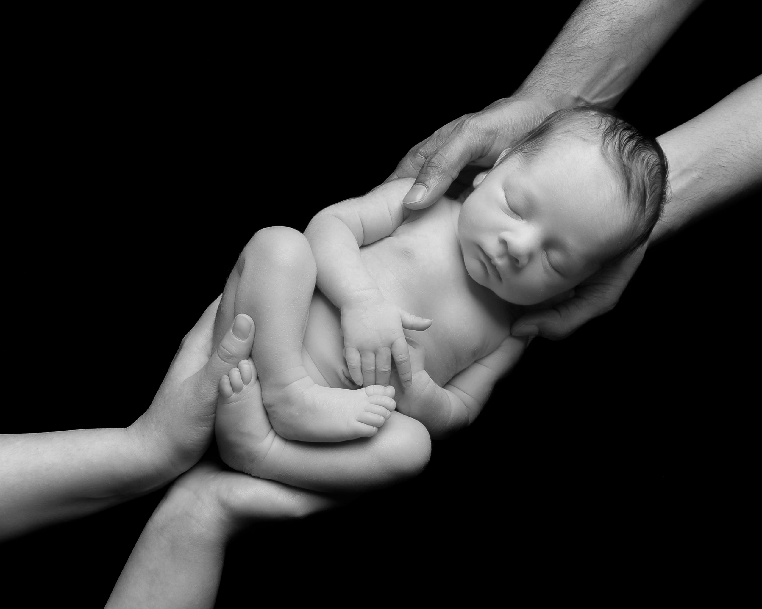 Newborn baby photographed layingg on s flat surface with mam and dad cradling